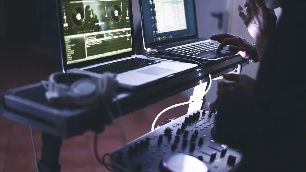 Karanlık bir odada ekranları açık müzik ekipmanı başındaki bir kişi
